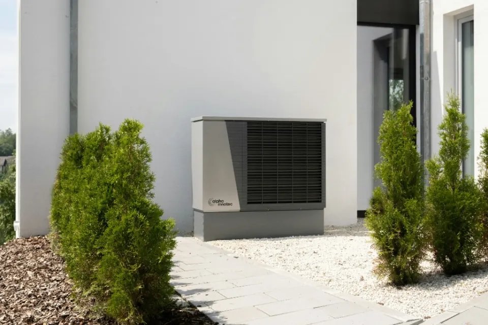 Outdoor air conditioning unit installed against a white wall on a gravel base