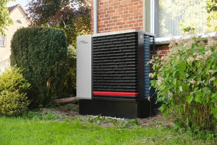 Outdoor air source heat pump installed beside a brick house with hedging